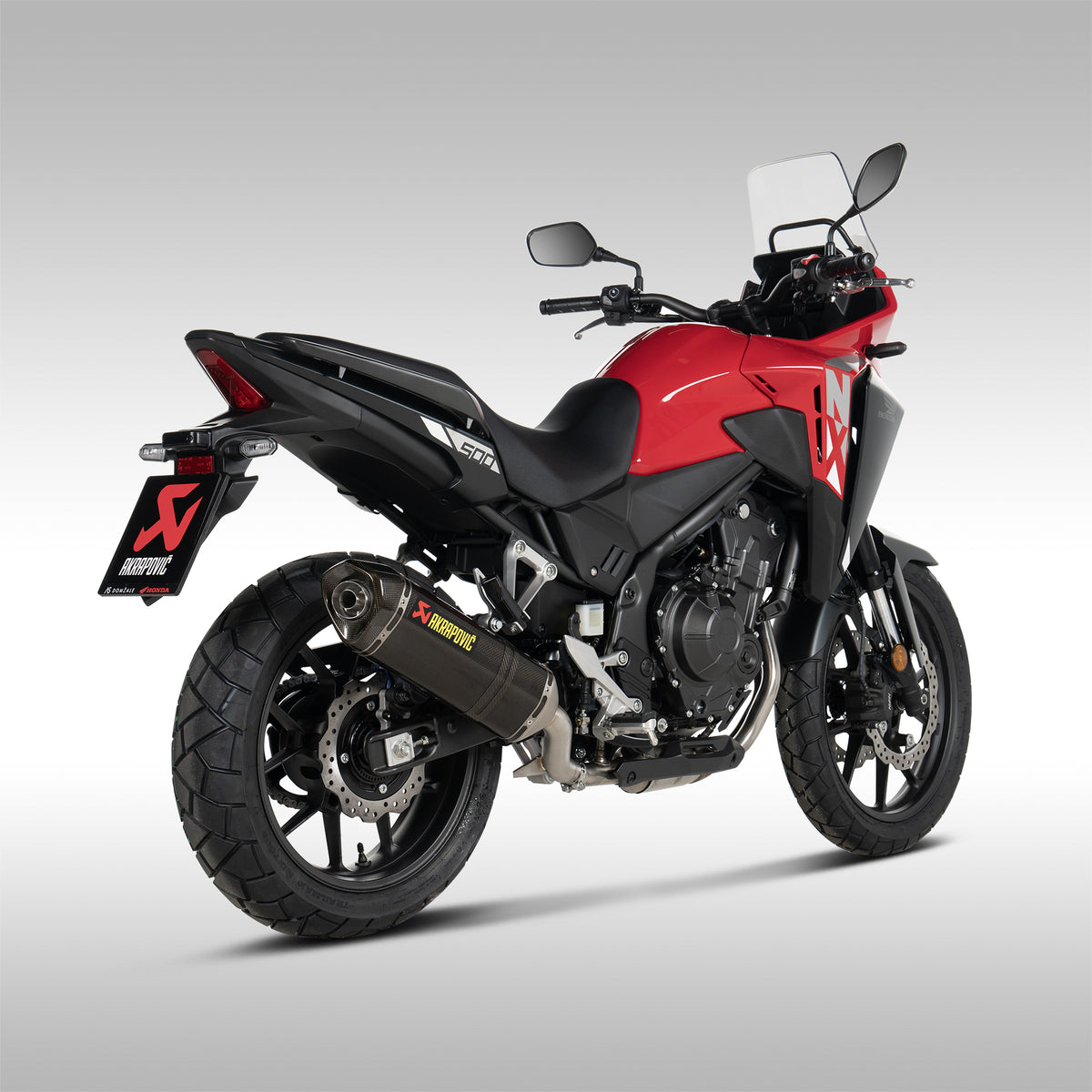 Akrapovic carbon fiber slip-on exhaust for Honda NX500 motorcycle, showing the black muffler installed on a red NX500, rear 3/4 view.