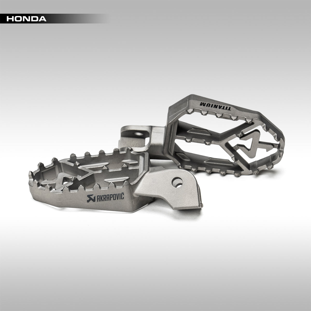 Metal foot pegs with 'Honda' branding on a gray background