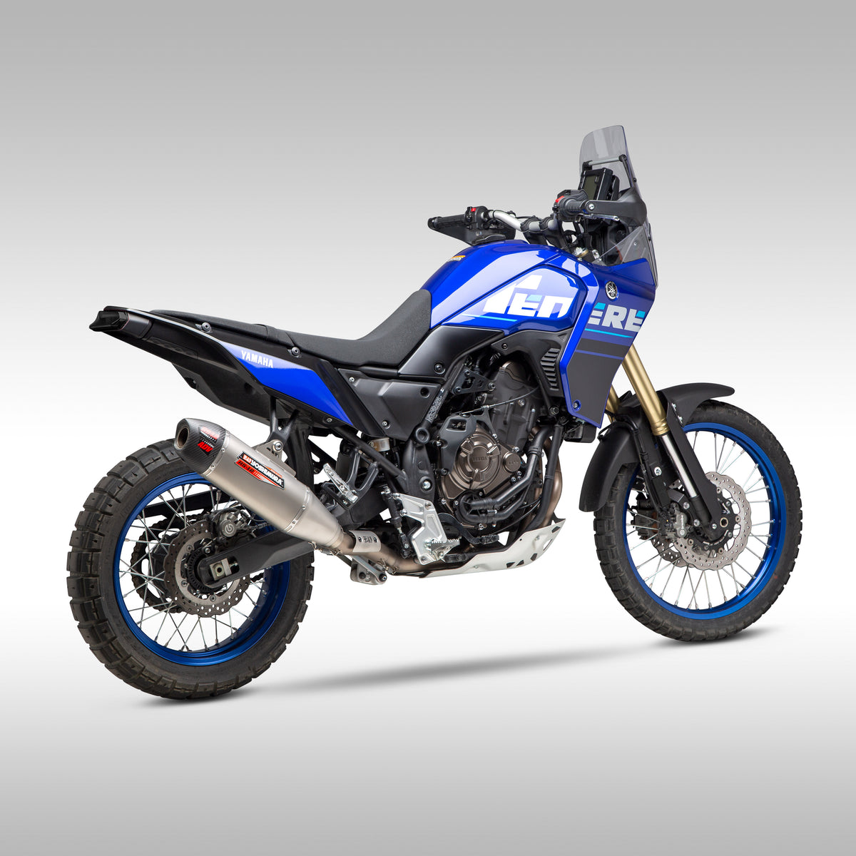 Blue Tenere 700 with Yoshimura RS-12 exhaust, rear three quarter on gray background.